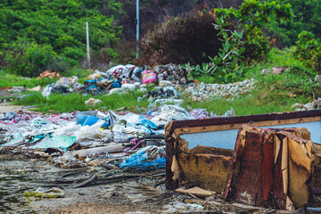 Spilled recycling man made garbage in park forest outside city. Used dirty waste plastic bags, carton paper, old discarded furniture. Environmental total pollution, ecological problem, global warming