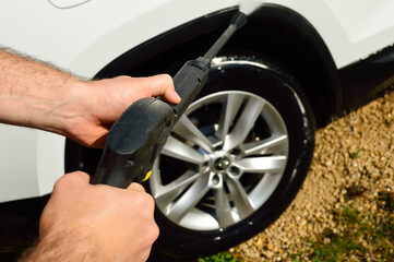 close-up - a high-pressure car wash pistol in the hands of a man, washes the wheels of a white car