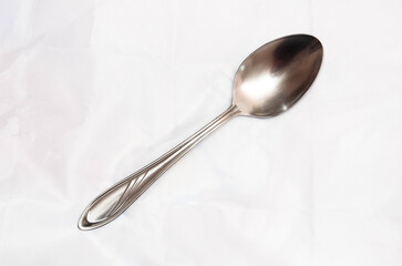 A steel teaspoon lies on a light background.