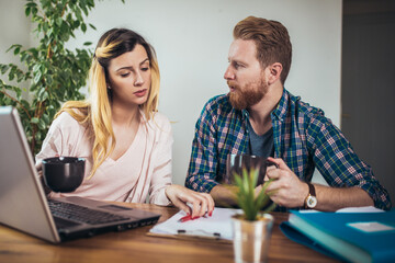 Young couple embracing and paying household bills or taxes on laptop online at home