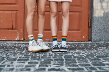 Close up of legs of young female couple wearing rainbow colored socks, standing together in front of the door outdoors