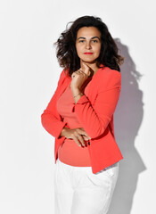 Self-confident business woman in elegant coral shirt, jacket and white pants listens intently holding hand at her chin