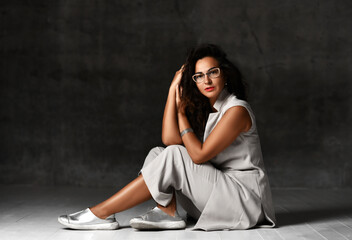 Charming woman in stylish glasses, trendy wide leg capri cropped pants, sleeveless jacket and silver shoes sits on the floor