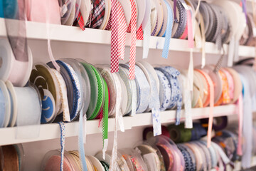Bobbins with various colorful ribbons on counter in store. Needlework and sewing supplies