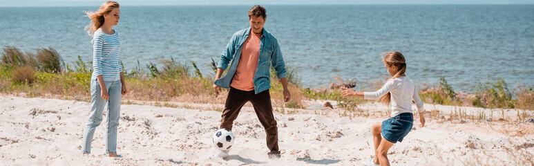 Horizontal crop of family playing football on beach during weekend