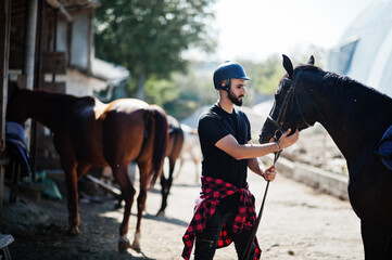 Arab tall beard man wear in black helmet with arabian horse.