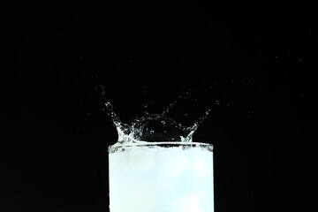 Splash from ice cube in a glass of water, isolated on the black background - obrazy, fototapety, plakaty