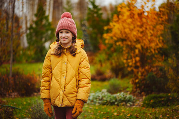 cute kid girl walking in autumn garden or park, wearing warm stylish clothes