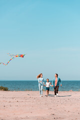 Selective focus of woman with kite walking near daughter and husband on beach
