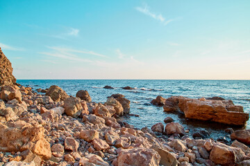 Fototapeta na wymiar Summer scenery. Virgin nature panorama. Nude beach. Relaxation. Stone coastline. Calming sea water. Blue evening sky