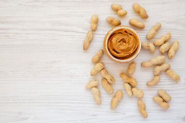 Jar full of peanut butter on a white wooden background, top view. Flat lay, overhead, from above. Copy space.