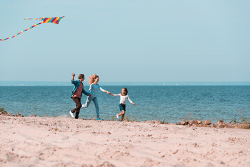 Selective focus of family holding hands while running with kite on seaside