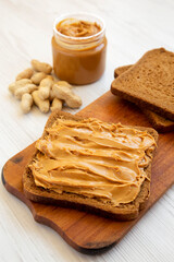 Piece of Bread with Peanut Butter on a rustic wooden board on a white wooden table, low angle view. Close-up.