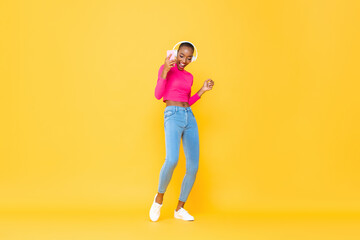 Fototapeta na wymiar Joyful portrait of dancing happy African American woman wearing headphones listening to music from smartphone on colorful yellow studio isolated background