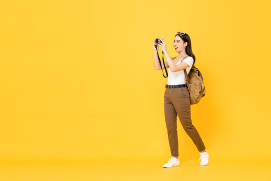 Young Asian tourist woman taking photo with camera isolated on yellow background