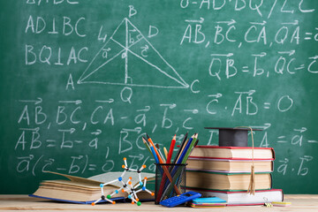 Education and sciences concept - books on the teacher desk in the auditorium, chalkboard on the background.