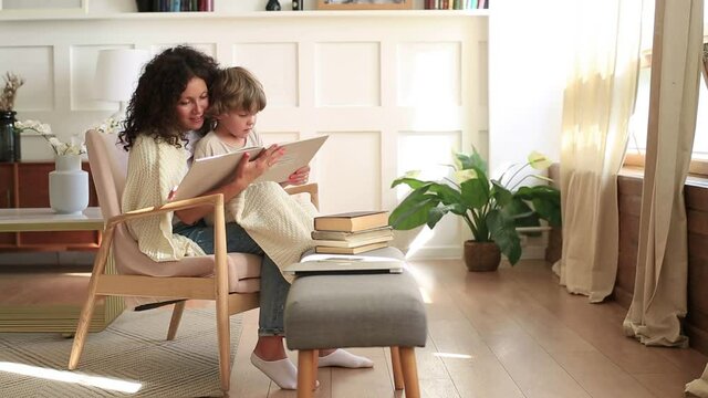 Mom and little son in a chair together reading a book at home. Quiet and comfort at home, a concept on the theme of family and family values.