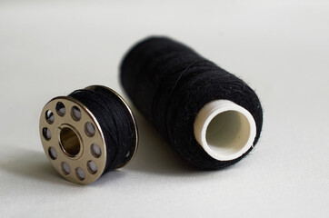 Sewing supplies. Bobbin and spool with black threads on a gray background