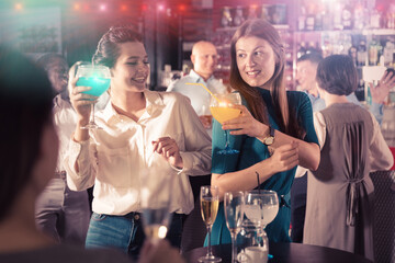 Portrait of two young women drinking cocktails and talking on corporate party