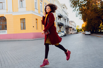 Full length image of  young  black lady in  hat and wool coat jumping  over street background.  Autumn and winter concept.