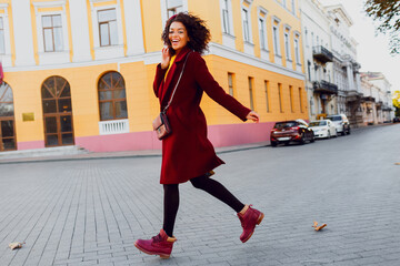 Wonderful young  black lady in  hat and wool coat jumping  over street background.  Autumn and winter concept.