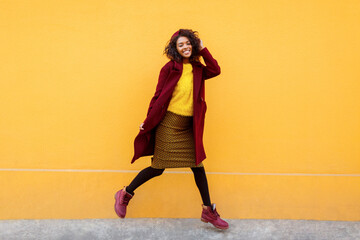 Full length image of excited black woman jumping with happy face expression on yellow background.