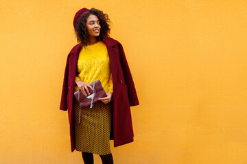 Fashionable black girl in amazing winter outfit and  accessories  posing on yellow background.  Wavy hairs.  Fluffy sweater.