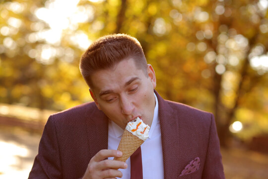 Happy Young Businessman Man Eating Ice Cream With Big Appetite In Autumn Park On Background Of A Yellow Trees.