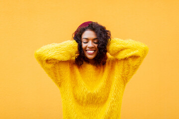 black  smiling woman  with clothes eyes  playing with her curly hair on yellow background in cute fluffy  sweater and   Burgundy beret.