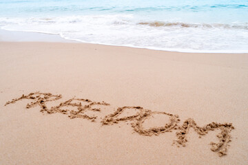 Freedom word hand drawn on sand summer beach.