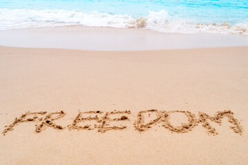 Fototapeta na wymiar Freedom word hand drawn on sand summer beach.
