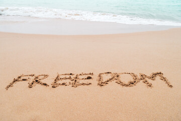 Freedom word hand drawn on sand summer beach.