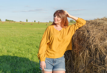 Naklejka na ściany i meble female model plus size on a field with haystacks, a beautiful young woman with brown hair in short shorts and a white shirt, harvest concept