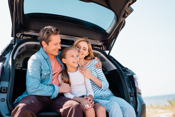 Man hugging wife and kid while sitting in trunk of car outside