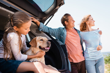 Selective focus of child and golden retriever sitting in car trunk near parents outdoors © LIGHTFIELD STUDIOS