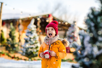 Young boy holding Santa's cup of cacao with marshmallows standing on a fake ice rink.