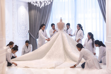 Team of female dressmaking workers preparing a large haute couture wedding dress on a mannequin in a bridal design studio. - obrazy, fototapety, plakaty