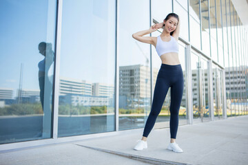 Fototapeta na wymiar Attractive fit young sportsgirl doing stretching exercises standing next to glass building