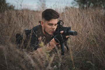 Fototapeta premium Young soldier in black uniform lying down and aiming an assault rifle.