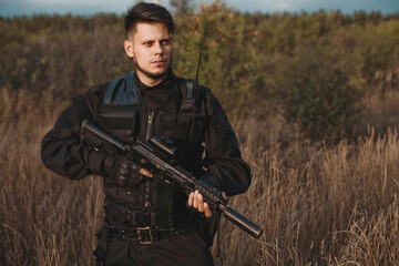 Young soldier in black uniform with an assault rifle. Toned.