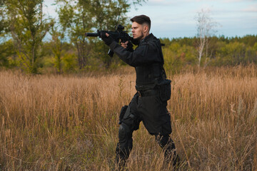 Young soldier in black uniform aiming an assault rifle.