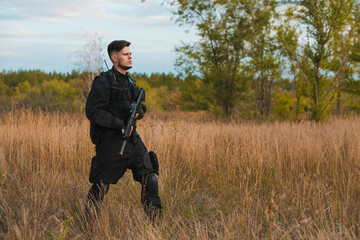 Young soldier in black uniform with an assault rifle. Copy space.