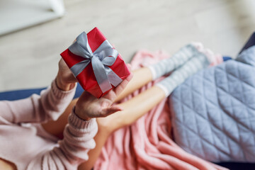 Cozy warm holiday mood. Young woman holding gift box. Top view.  Wearing pink trendy pullover, winter stylish socks.