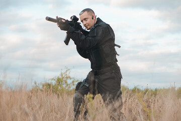 Special force soldier in black uniform aiming an assault rifle.