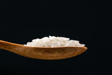 Side view of Jasmine rice in a wooden spoon on black background.