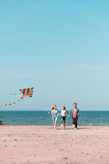 Selective focus of woman holding kite while running with family on beach