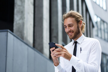 Portrait of a successful young businessman. A curly-haired man in a white shirt with a telephone against the background of a modern business center.