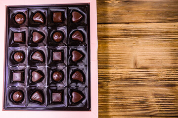 Heap of chocolate candies in a brown box on wooden table. Top view
