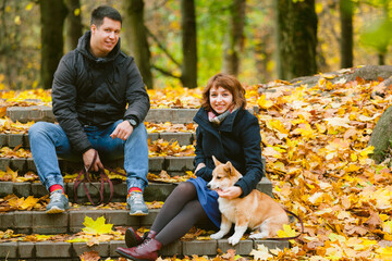 Happy couple playing with Corgi dog in sunny autumn park. Man and woman having fun outdoors with pet.