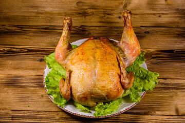 Plate with roasted whole chicken and lettuce leaves on a wooden table